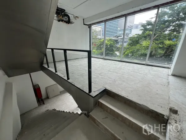 零售空间 出租在Bang Rak, Bangkok - 楼梯平台通向夹层，配整面落地窗与城市景致。
