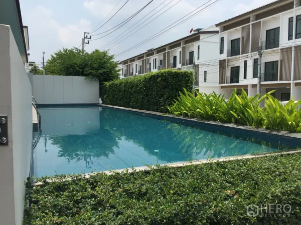 Townhouse for rent in Bang Kapi, Bangkok - Community swimming pool bordered by hedges and modern three-storey townhouses.