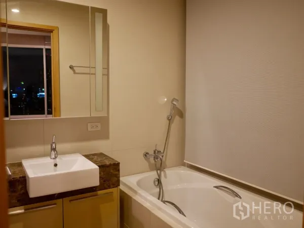 Condominium for rent in Watthana, Bangkok - Bathroom with bathtub, handheld shower and vanity with mirror.