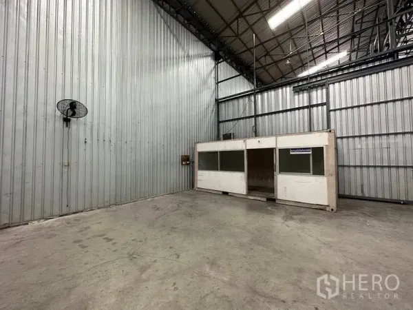 Warehouse for rent in Pak Kret, Nonthaburi - Corner of the warehouse with wall-mounted ventilation fans and a small internal office cabin.