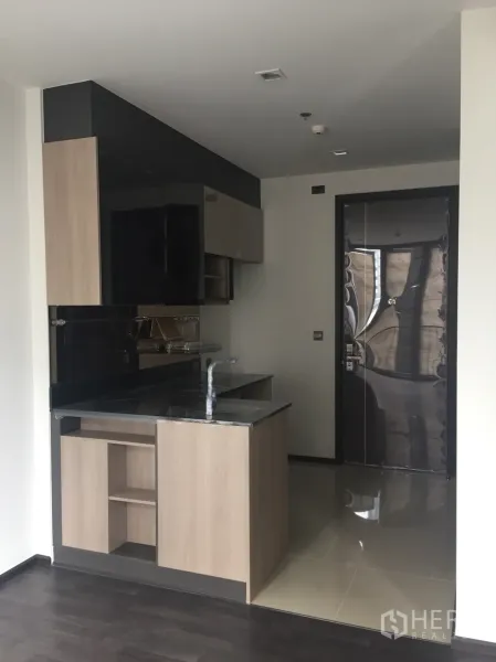 Condominium for sale in Din Daeng, Bangkok - Compact condo kitchen with black stone countertop, light wood cabinets, and entry door in a modern Din Daeng unit.