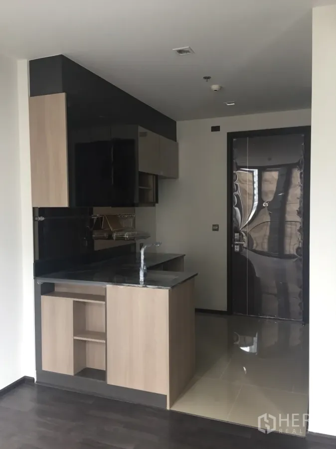 Condominium for sale in Din Daeng, Bangkok - Compact condo kitchen with black stone countertop, light wood cabinets, and entry door in a modern Din Daeng unit.