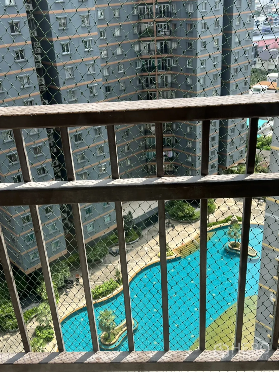 Condominium for rent in Yan Nawa, Bangkok - Balcony view through safety net overlooking a large outdoor swimming pool and towers.