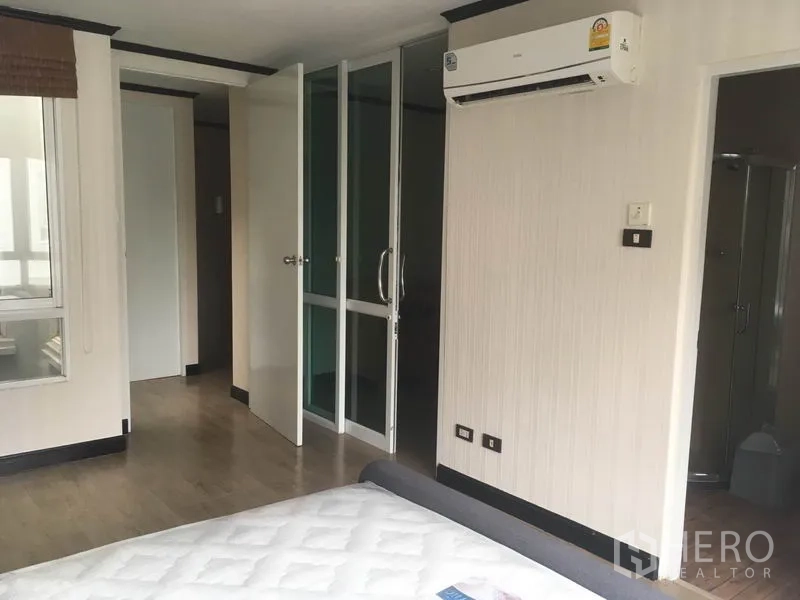 Townhouse for rent in Din Daeng, Bangkok - Bedroom detail showing air conditioner, glass wardrobe doors and wood flooring.