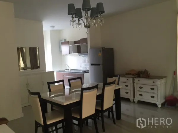 Townhouse for rent in Watthana, Bangkok - Dining area with six-seat table, chandelier, and open kitchenette with fridge and cabinets.