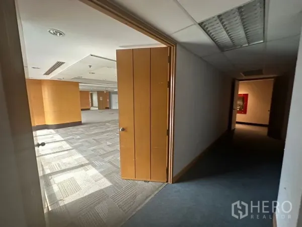 Office Space for rent in Khlong Toei, Bangkok - Doorway opening from a dim hallway into a bright open-plan office with carpet tiles and wood accents.