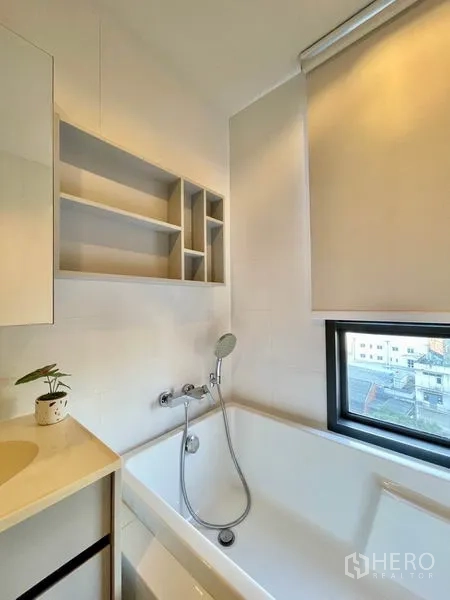 Condominium for rent or sale in Watthana, Bangkok - Bathroom with soaking bathtub, window and open shelving.