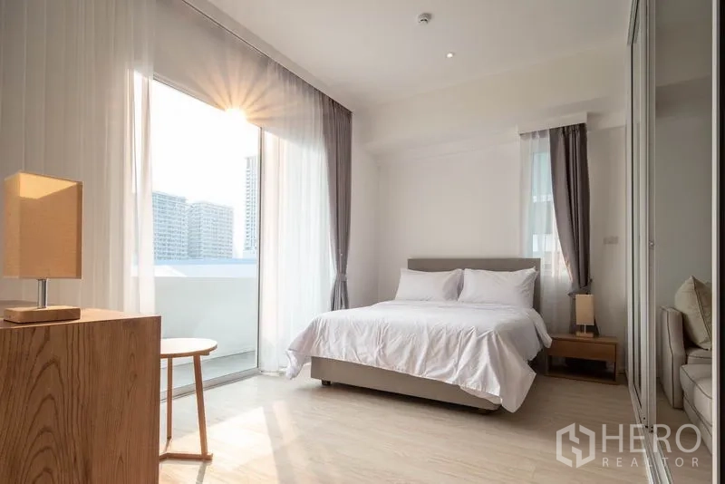 Condominium for rent in Khlong Toei, Bangkok - Sunlit bedroom with double bed, sheer curtains and access to a balcony.