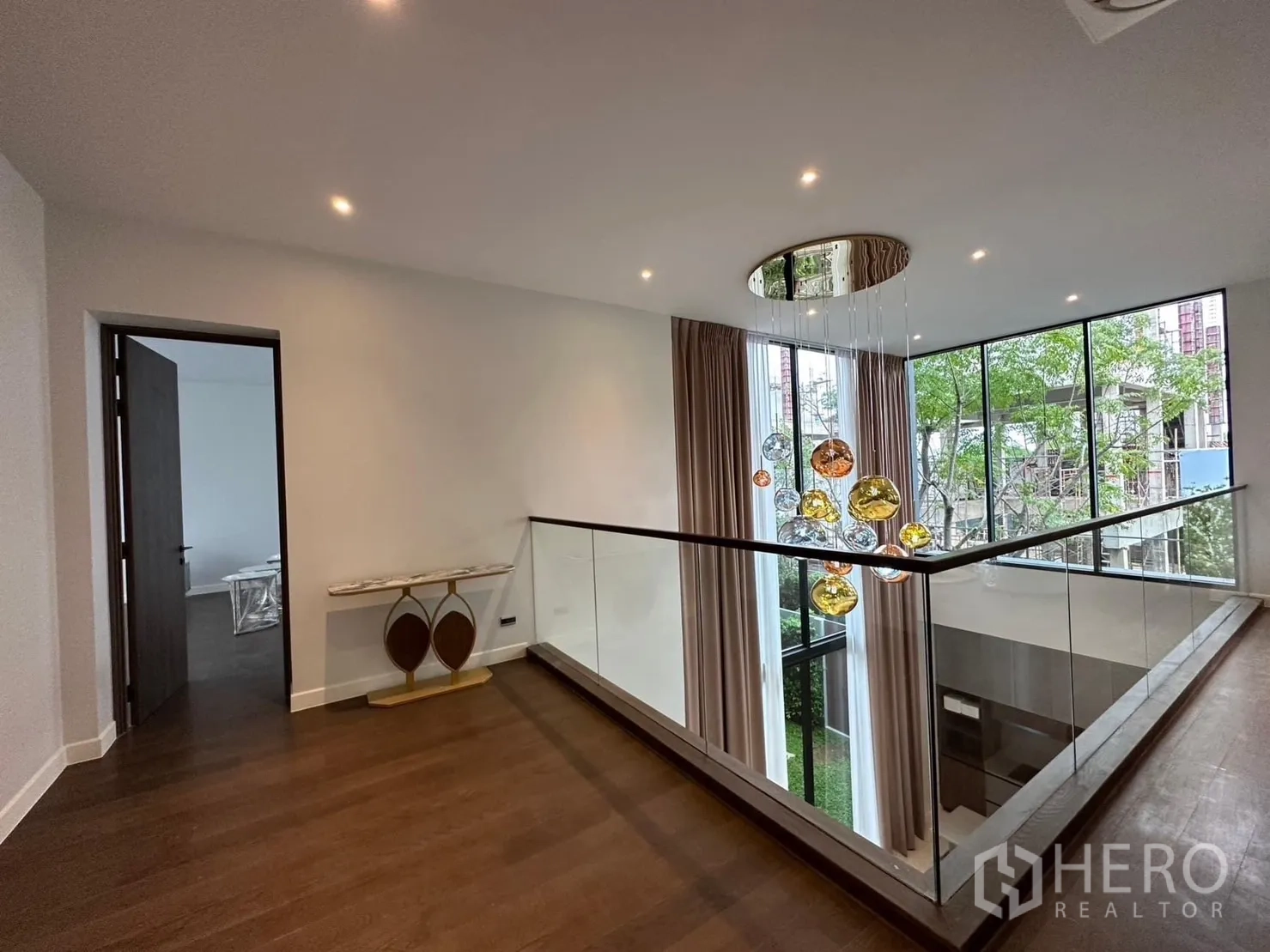 Detached House for rent - Upper landing with glass balustrade and statement pendant lights beside tall windows.