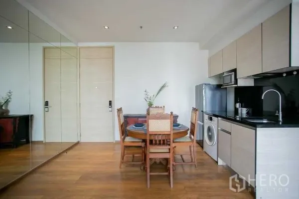 Condominium for sale in Khlong Toei, Bangkok - Mirrored wall reflecting the dining set and entry doors in a bright condo interior.