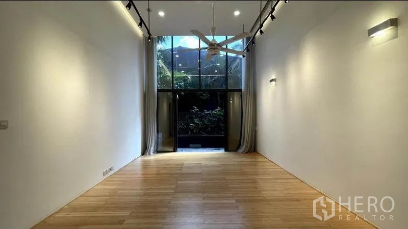 公寓 出租在Watthana, Bangkok - 狭长客厅配落地窗与吊扇，窗帘拉开通向绿意阳台/庭院