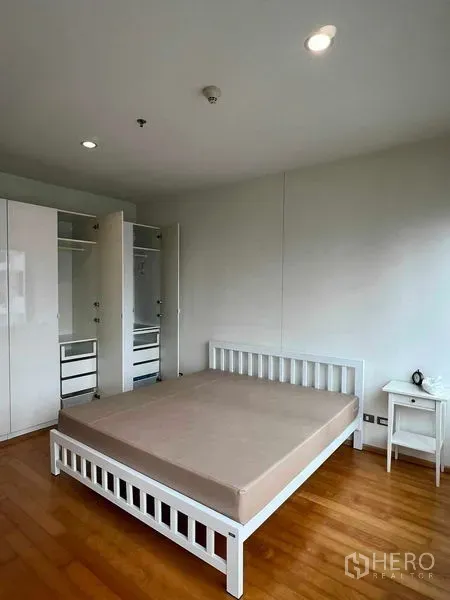 Condominium for rent in Ratchathewi, Bangkok - Primary bedroom with white bed frame, wardrobes, and warm wooden flooring.