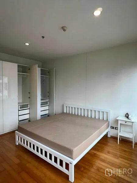 Condominium for rent in Ratchathewi, Bangkok - Primary bedroom with white bed frame, wardrobes, and warm wooden flooring.