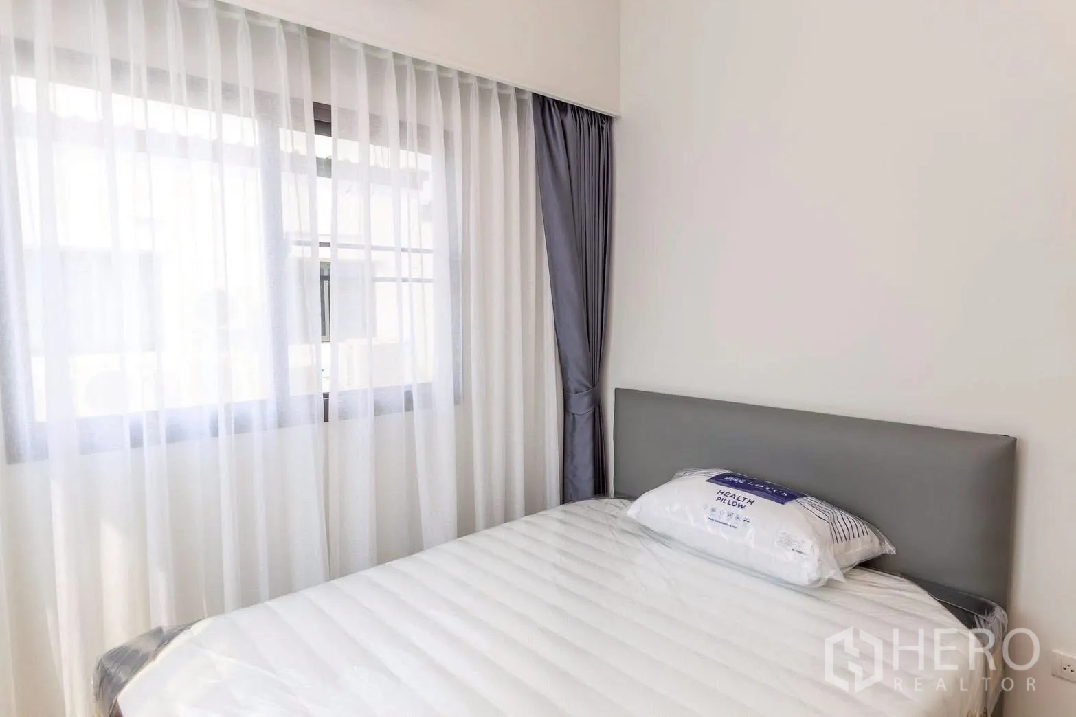 Townhouse for rent or sale in Bang Phli, Samut Prakan - Secondary bedroom with gray headboard, white sheer curtains and soft natural light.