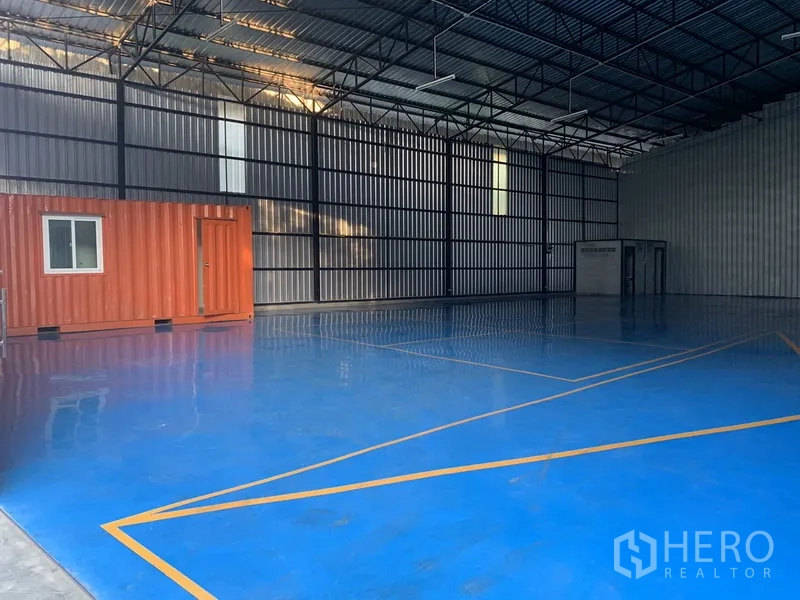 Warehouse for rent in Khan Na Yao, Bangkok - Open storage space featuring a blue epoxy floor and an orange container-style office inside the warehouse.