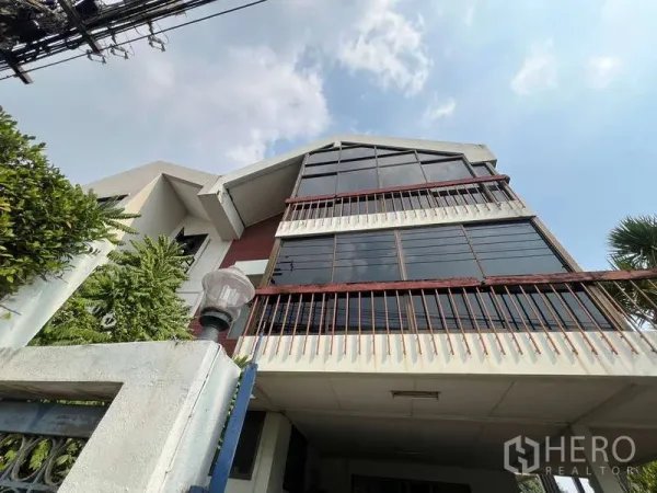 独立式住宅 出售在Suan Luang, Bangkok - Suan Luang 多层独栋别墅，玻璃三角立面与阳台，晴空下外观。