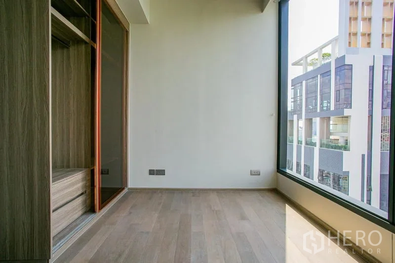 Condominium for rent in Watthana, Bangkok - Compact bedroom or study with built-in wardrobe and large window overlooking a modern building.