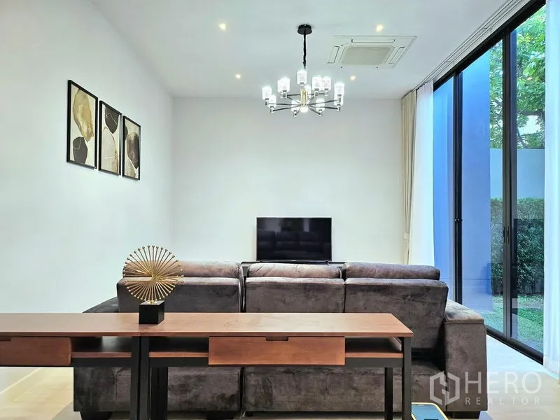 บ้าน ให้เช่าในBang Kapi, Bangkok - ห้องนั่งเล่น โซฟาตัวแอลสีเทา ทีวี และประตูกระจกเลื่อนออกสู่สวน