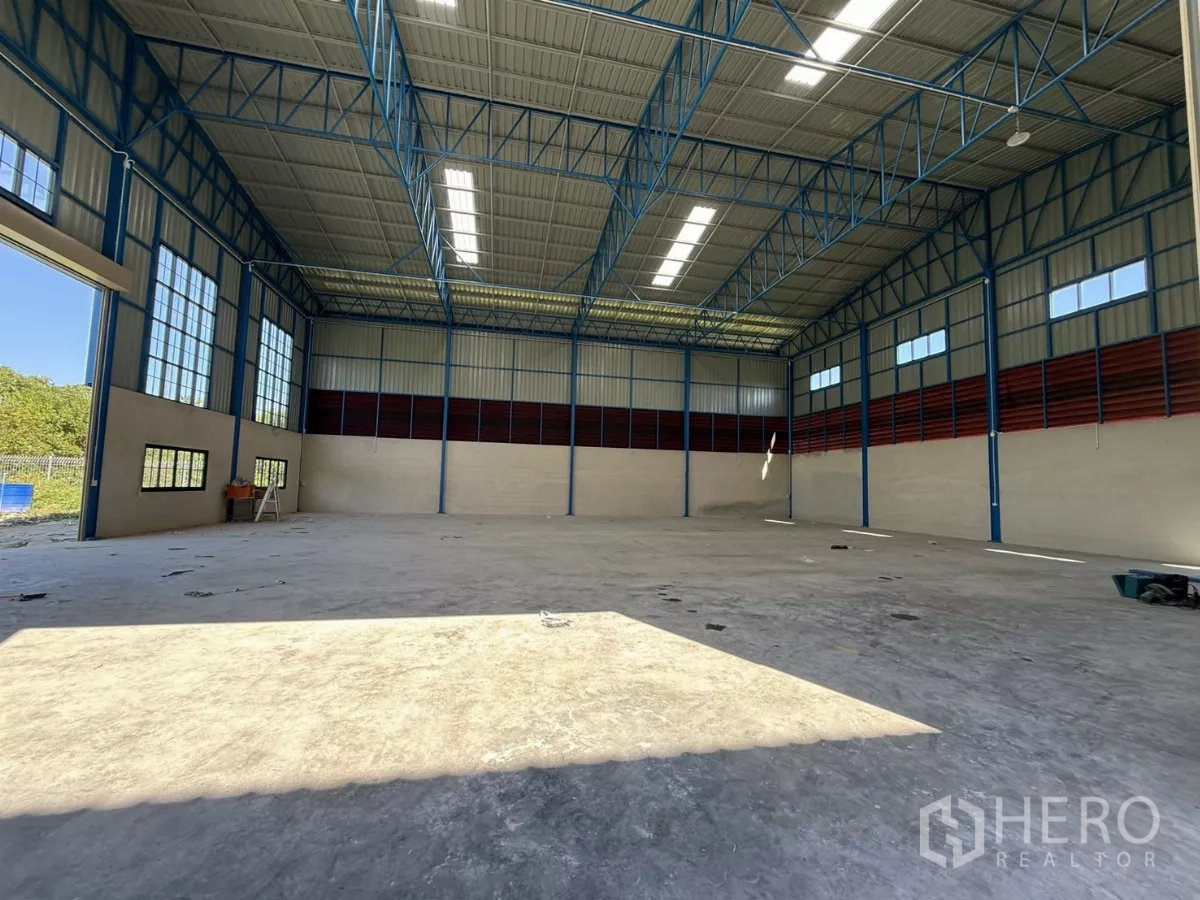Warehouse for rent in Lam Luk Ka, Pathum Thani - Wide interior facing the loading entrance with red louver cladding and concrete floor.