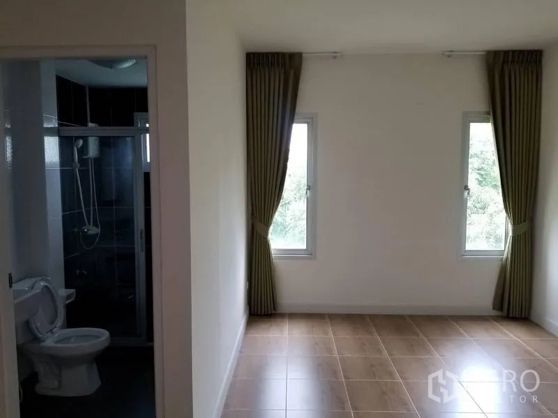 Townhouse for rent in Bang Kapi, Bangkok - Bedroom with two tall windows, curtains and an en-suite bathroom.