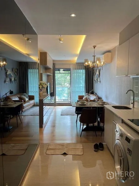 Condominium for rent in Watthana, Bangkok - Open-plan living and dining area with chandelier lighting, sofa, large windows, and kitchenette.