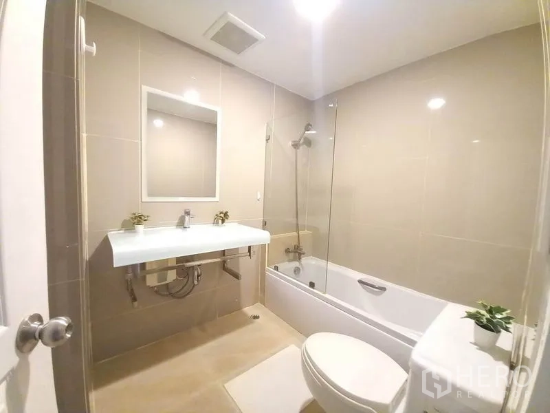 Condominium for rent in Khlong Toei, Bangkok - Modern bathroom with bathtub, glass screen and wall-mounted sink.