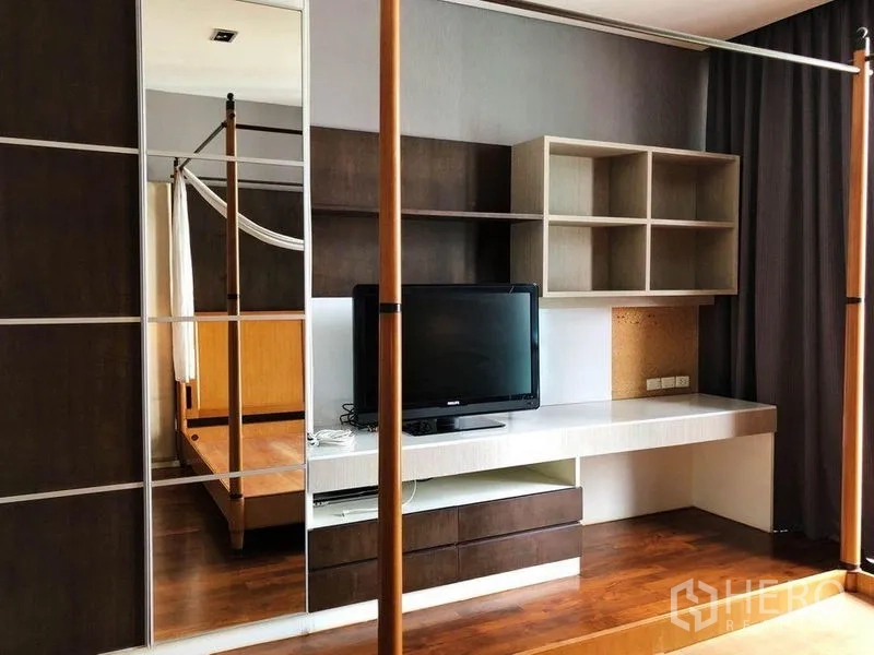 Condominium for rent in Khlong Toei, Bangkok - Master bedroom corner with desk and shelving, TV and mirrored wardrobe near a four-poster bed.