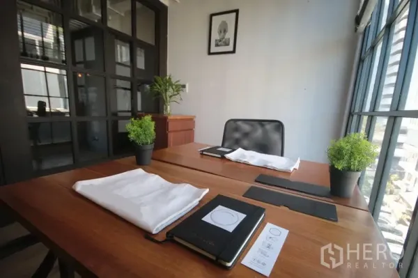 Office Space for rent in Khlong Toei, Bangkok - Sunlit worktable by floor-to-ceiling windows with potted plants and a city outlook.