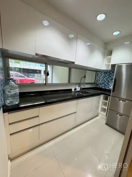 Townhouse for rent in Suan Luang, Bangkok - Bright modern kitchen with white cabinetry, black countertop, hob and fridge.
