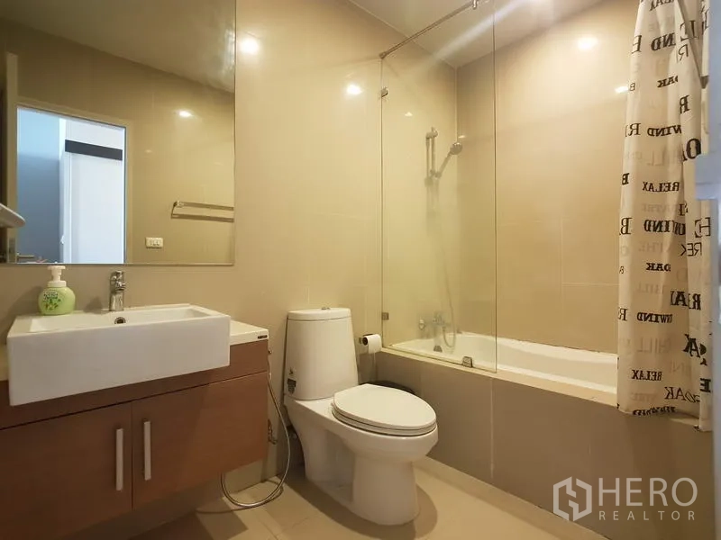 Condominium for rent in Bangkok - Contemporary bathroom with bathtub and shower, glass partition, vanity and toilet.