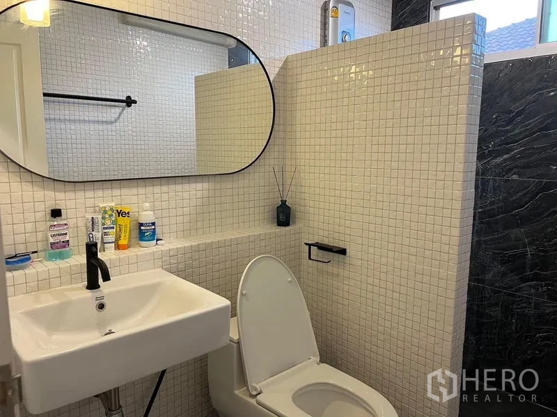 Detached House for sale in Bang Kruai, Nonthaburi - Bathroom with white mosaic wall tiles, oval mirror, black fixtures and toilet.
