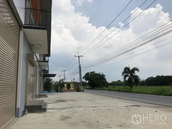 Factory for rent in Pathum Thani - Row of factory units with wide concrete apron facing a main road and green fields.
