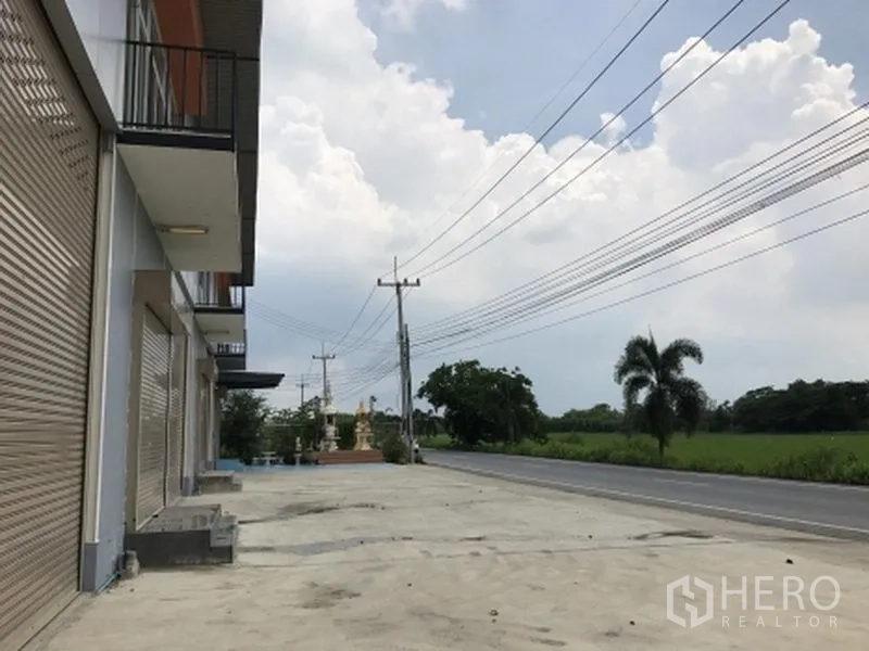 Factory for rent in Pathum Thani - Row of factory units with wide concrete apron facing a main road and green fields.