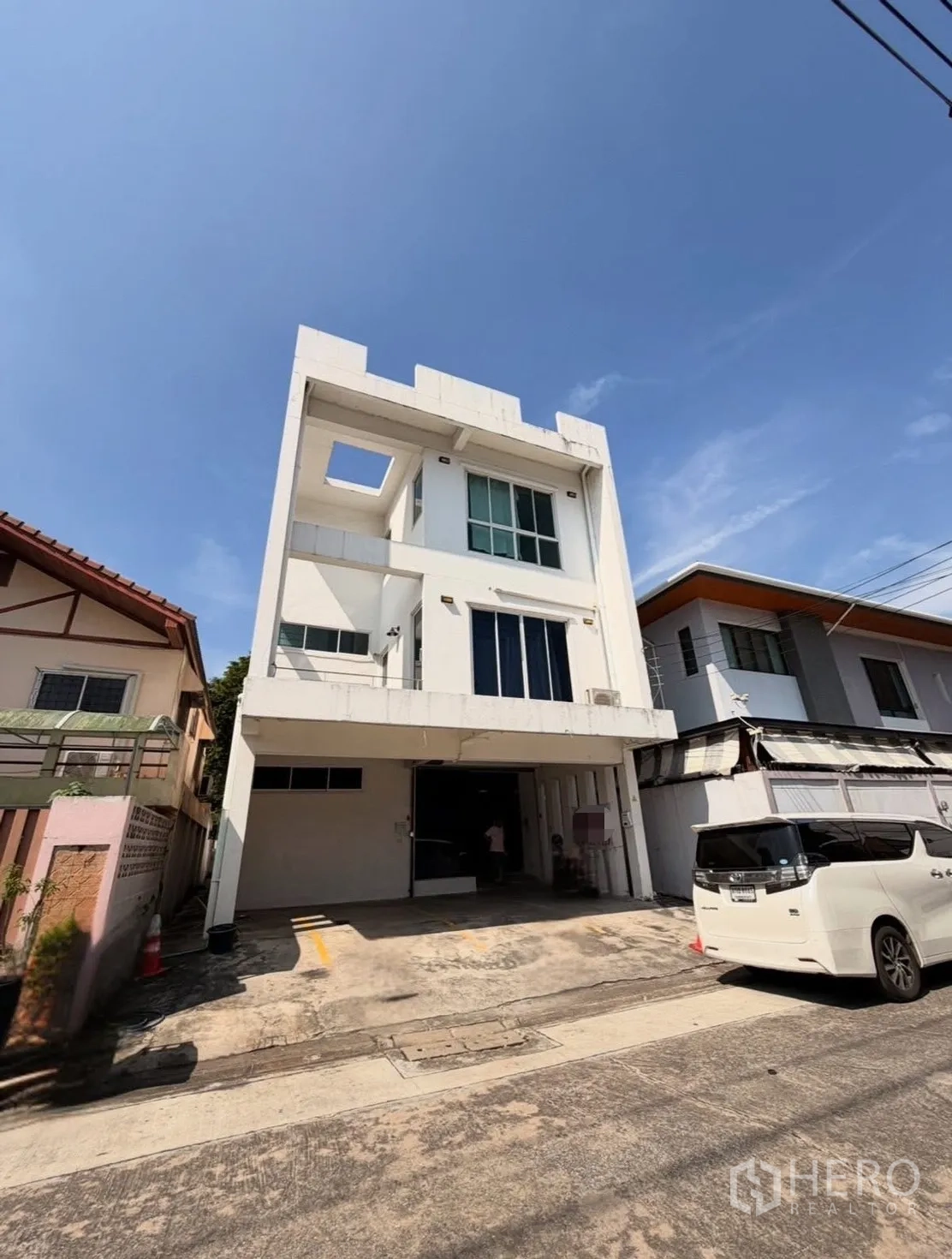 Home Office for rent in Huai Khwang, Bangkok - Street view of a four-storey white home office with on-site parking.