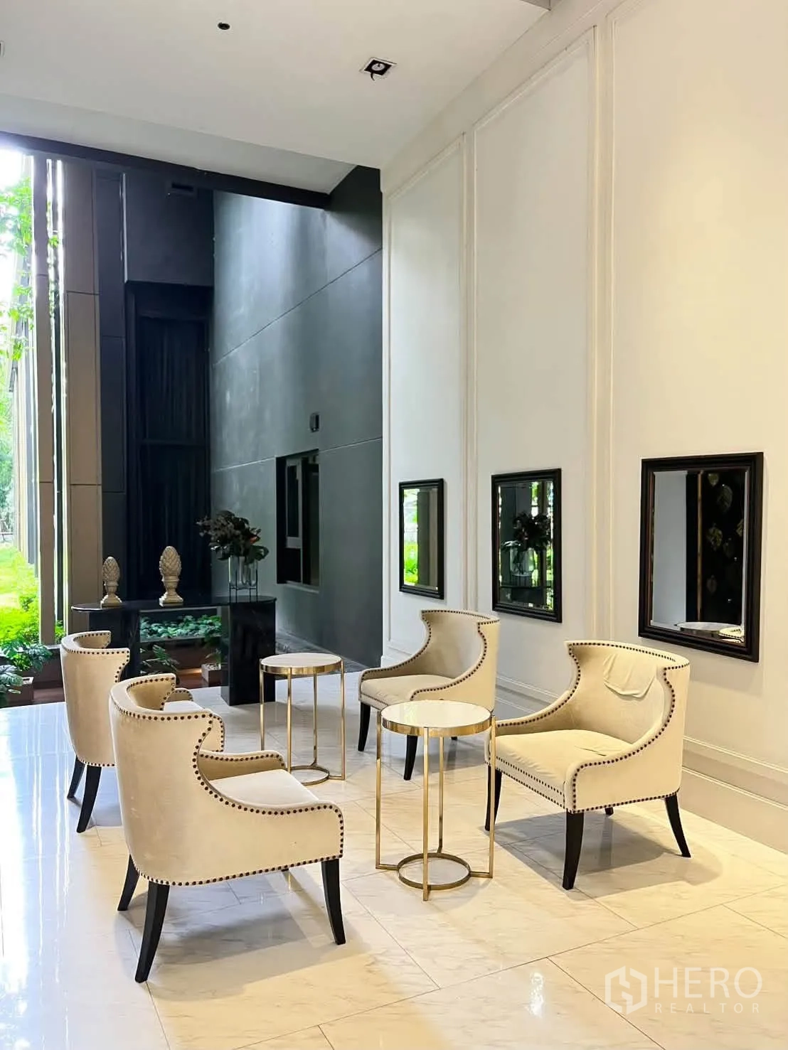 Condominium for rent in Pathum Wan, Bangkok - Seating corner with cream armchairs and gold side tables next to large windows.