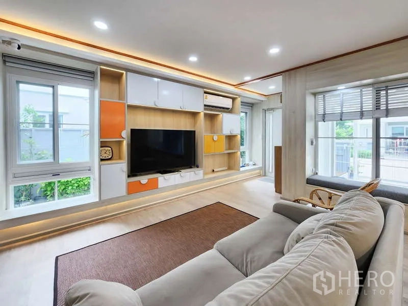 独立式住宅 出租或出售在Prawet, Bangkok - 客厅设定制电视墙、置物架与沙发，临园景窗。