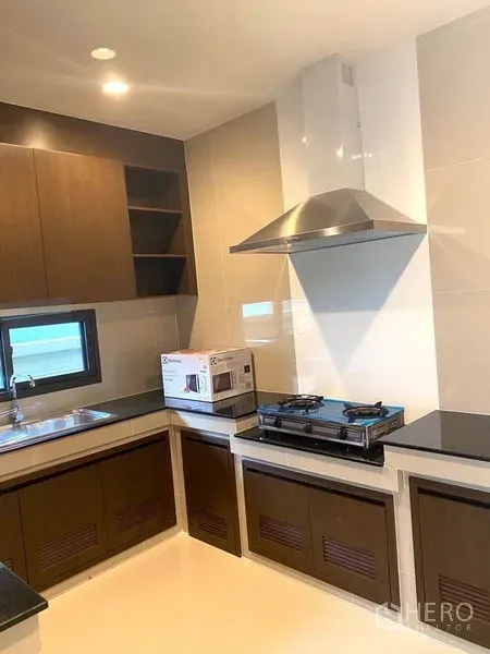 Detached House for rent in Saphan Sung, Bangkok - U-shaped kitchen with gas stove, stainless hood, sink and wood cabinetry.