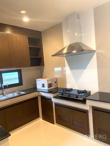 Detached House for rent in Saphan Sung, Bangkok - U-shaped kitchen with gas stove, stainless hood, sink and wood cabinetry.