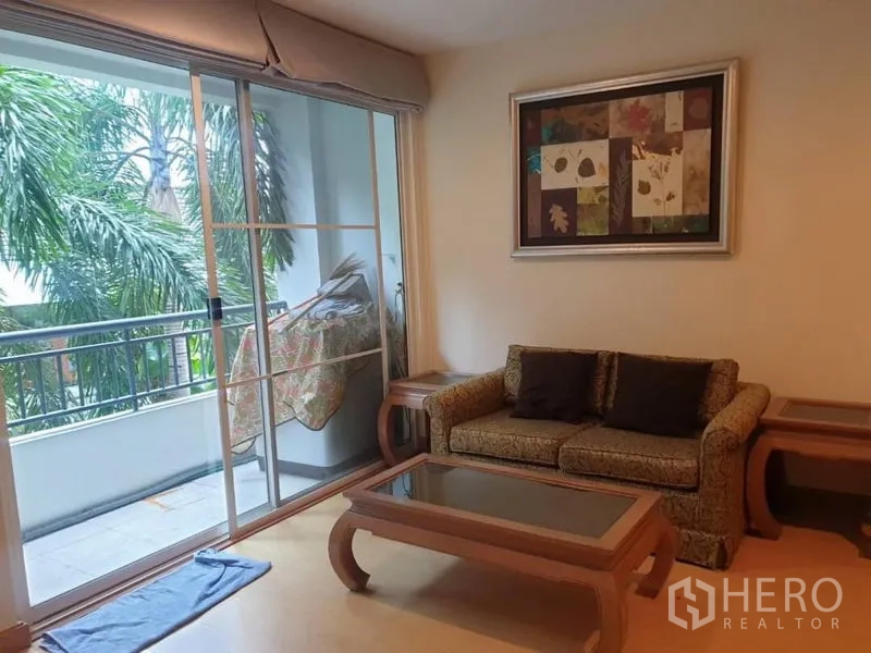 Condominium for rent in Watthana, Bangkok - Compact lounge with sofa and glass coffee table next to sliding doors to the balcony.