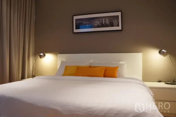Condominium for rent in Ratchathewi, Bangkok - Cozy bedroom with king-size bed, bedside lamps and framed cityscape artwork.