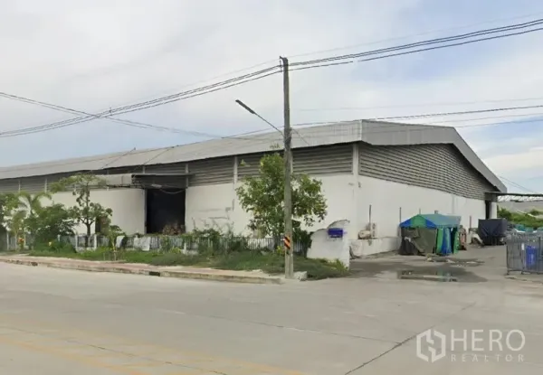 货栈 出租在Bang Pakong, Chachoengsao - 仓库转角外观，绿化围栏、服务庭院与临路门面。