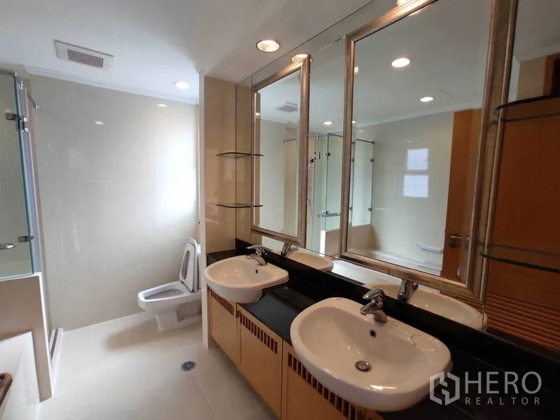 Condominium for rent in Khlong Toei, Bangkok - Bright bathroom with double sinks, large mirrors, glass shower and bathtub.
