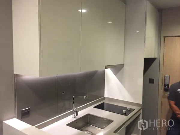 Condominium for rent in Watthana, Bangkok - Sleek galley kitchen with glossy white cabinets, stainless backsplash and sink.