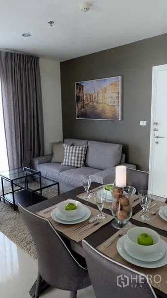 Condominium for sale in Khlong Toei, Bangkok - Bright living and dining area with gray sofa, glass coffee table and set dining table in a 2-bedroom condo near BTS On Nut.