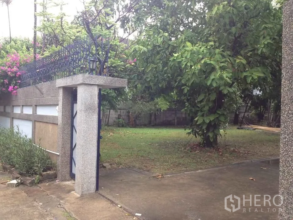 独栋房屋 for rent in Watthana, Bangkok - 带大门的入口通向草坪花园，沿围墙栽有树木。