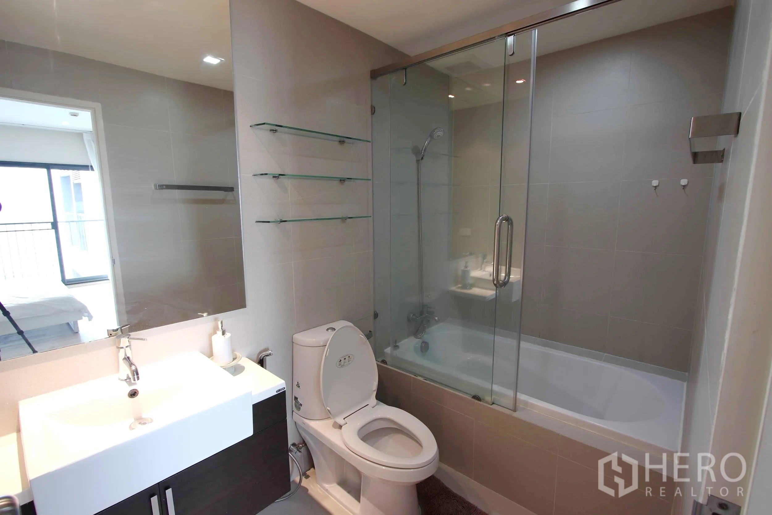 Condominium for rent in Khlong Toei, Bangkok - Contemporary bathroom featuring a wide vanity, toilet and bathtub with a glass shower screen.
