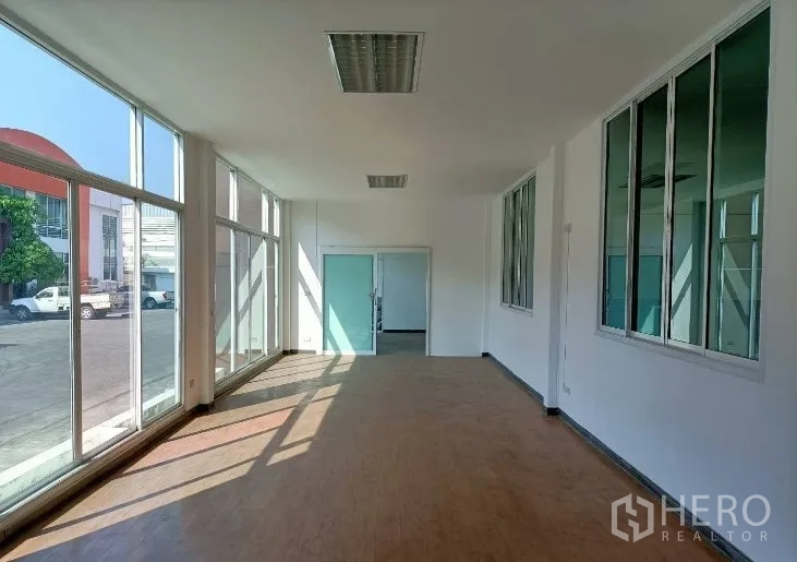 Factory for rent in Samut Prakan - Ground‑floor glass‑front office filled with natural light and wood‑look vinyl flooring.