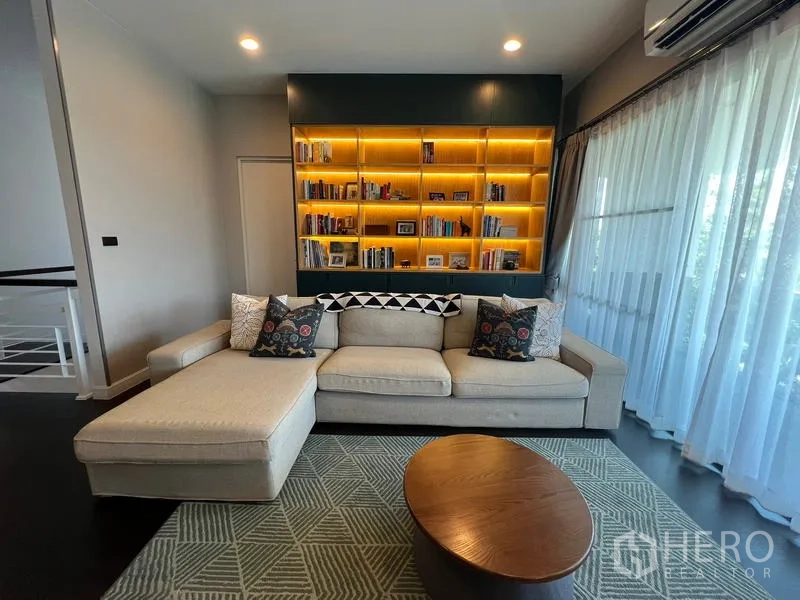 Detached House for rent in Bang Kapi, Bangkok - Upper-level lounge close-up showing sofa and backlit bookcase by the balcony doors.