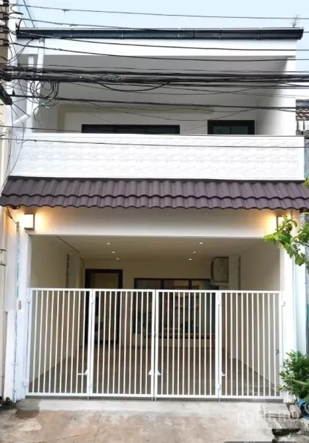 联排别墅 出租在Huai Khwang, Bangkok - 两层白色联排别墅外立面，带阳台与可上锁车位门，位于曼谷辉煌区。