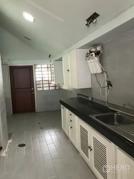 Detached House for rent in Lat Krabang, Bangkok - Galley kitchen with white cabinets, black countertop, stainless sink and grey tile walls.
